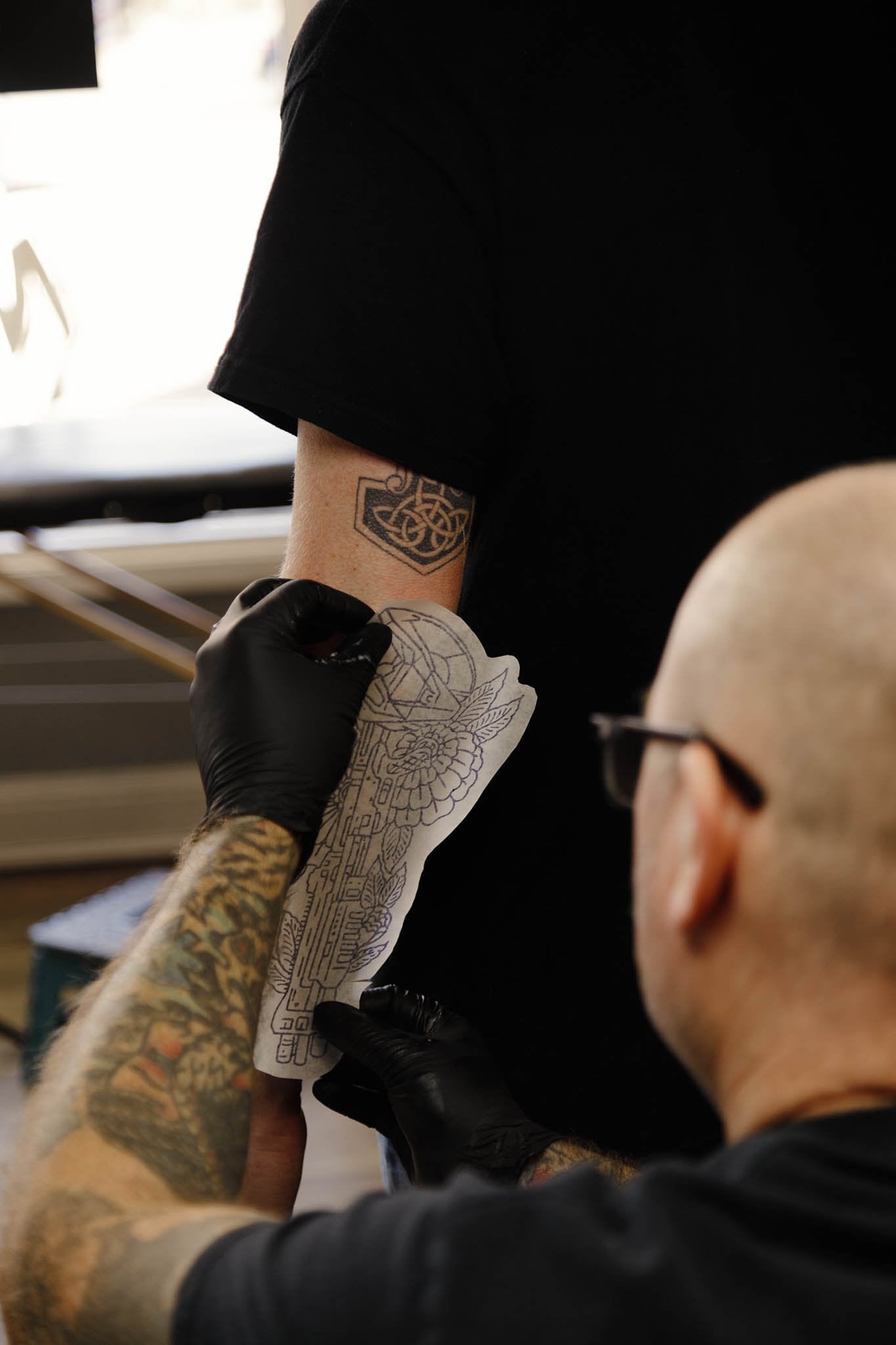 Tattoo artist preparing a stencil on a client’s forearm near a window