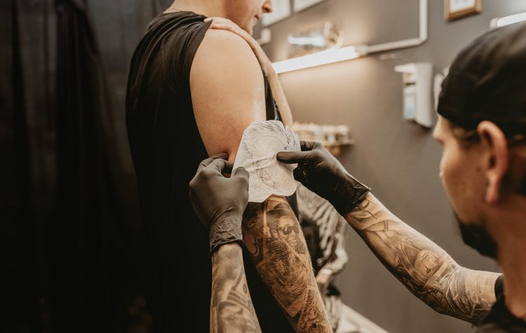 Tattoo artist aligning a stencil on a client’s upper arm